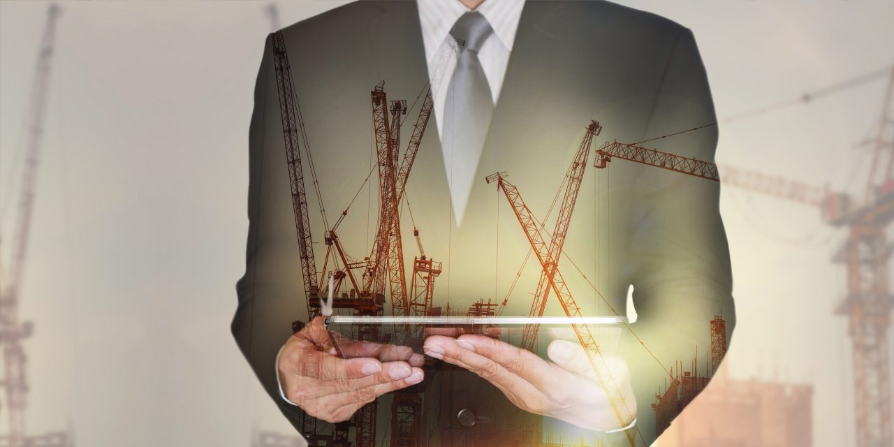 Double exposure of businessman hand hold tablet, construction crane, building and sunset in the evening as business, technology, communication and industry concept.